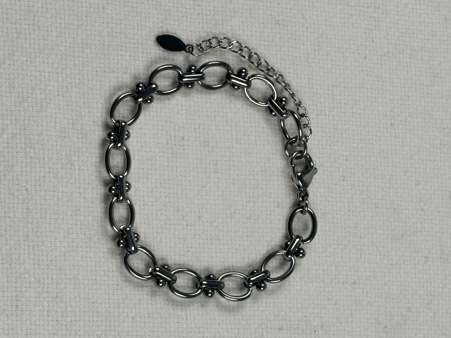 A silver chain bracelet with elongated oval links and a spring ring clasp, displayed on a textured off-white fabric background.