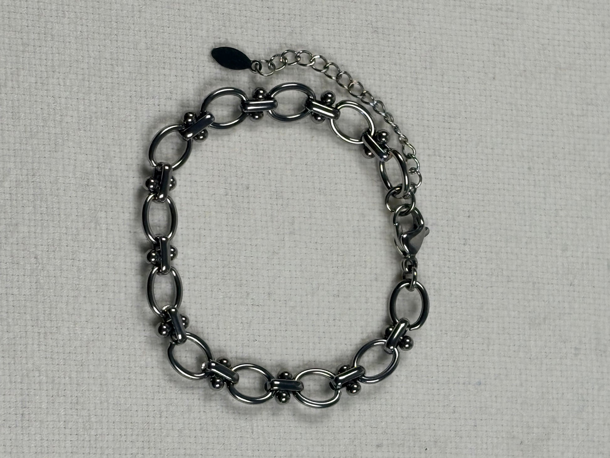 A silver chain bracelet with elongated oval links and a spring ring clasp, displayed on a textured off-white fabric background.