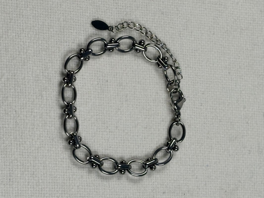A silver chain bracelet with elongated oval links and a spring ring clasp, displayed on a textured off-white fabric background.