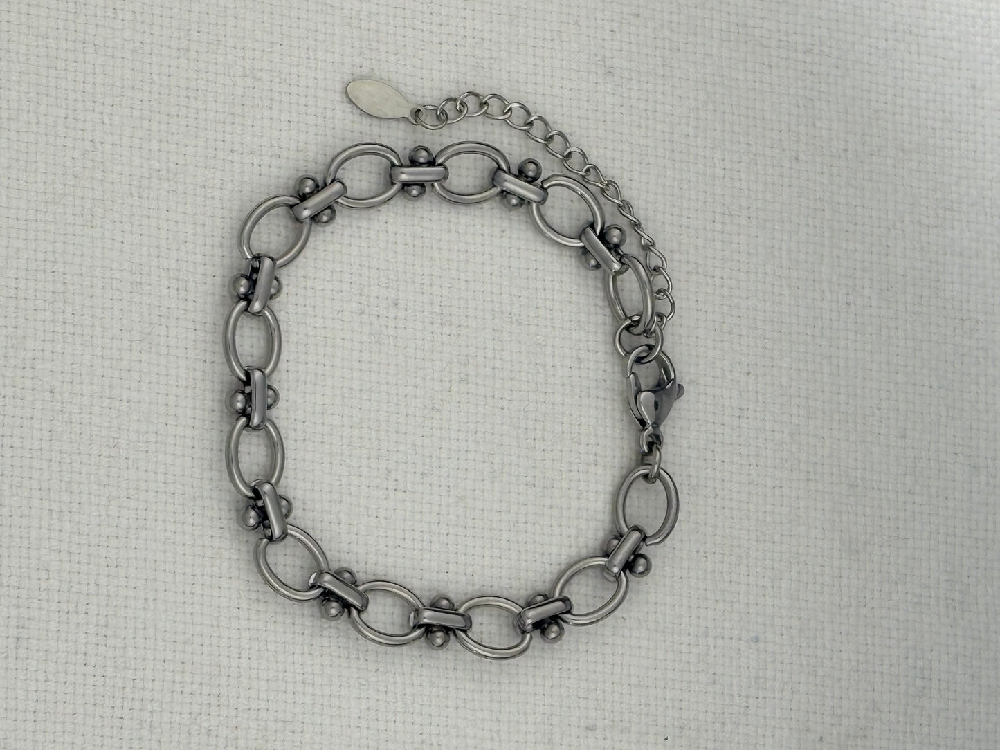 A silver-toned metal link bracelet with elongated oval links displayed on a textured off-white fabric background.