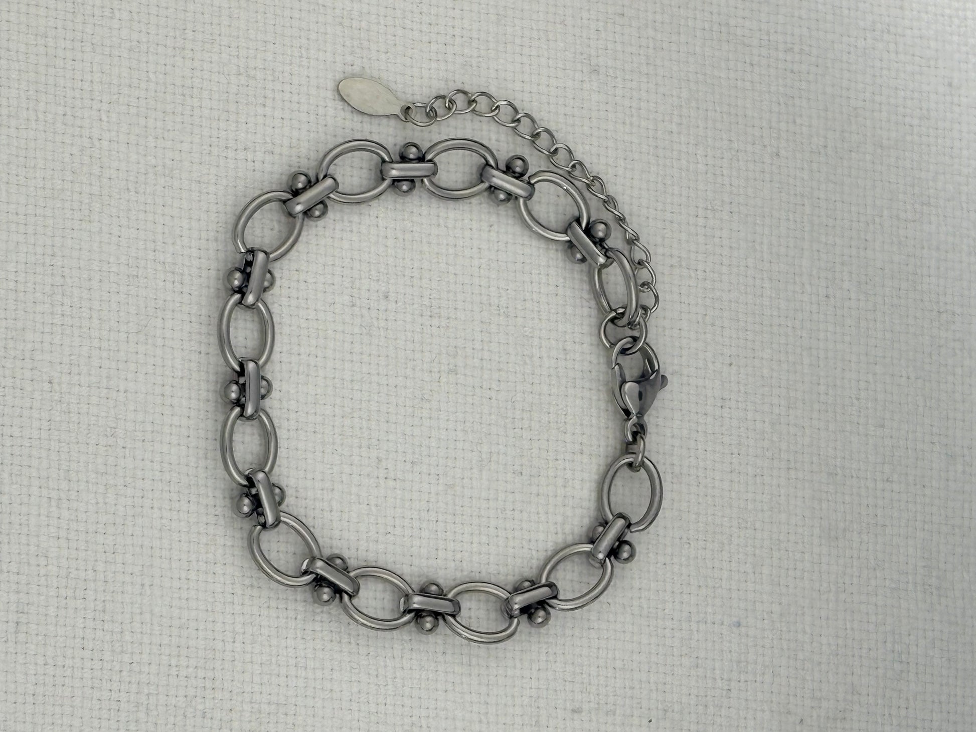 A silver-toned metal link bracelet with elongated oval links displayed on a textured off-white fabric background.