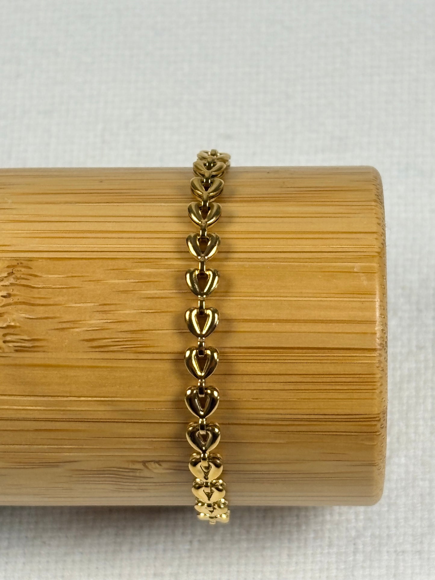 Gold bracelet on a wooden stand with a white background