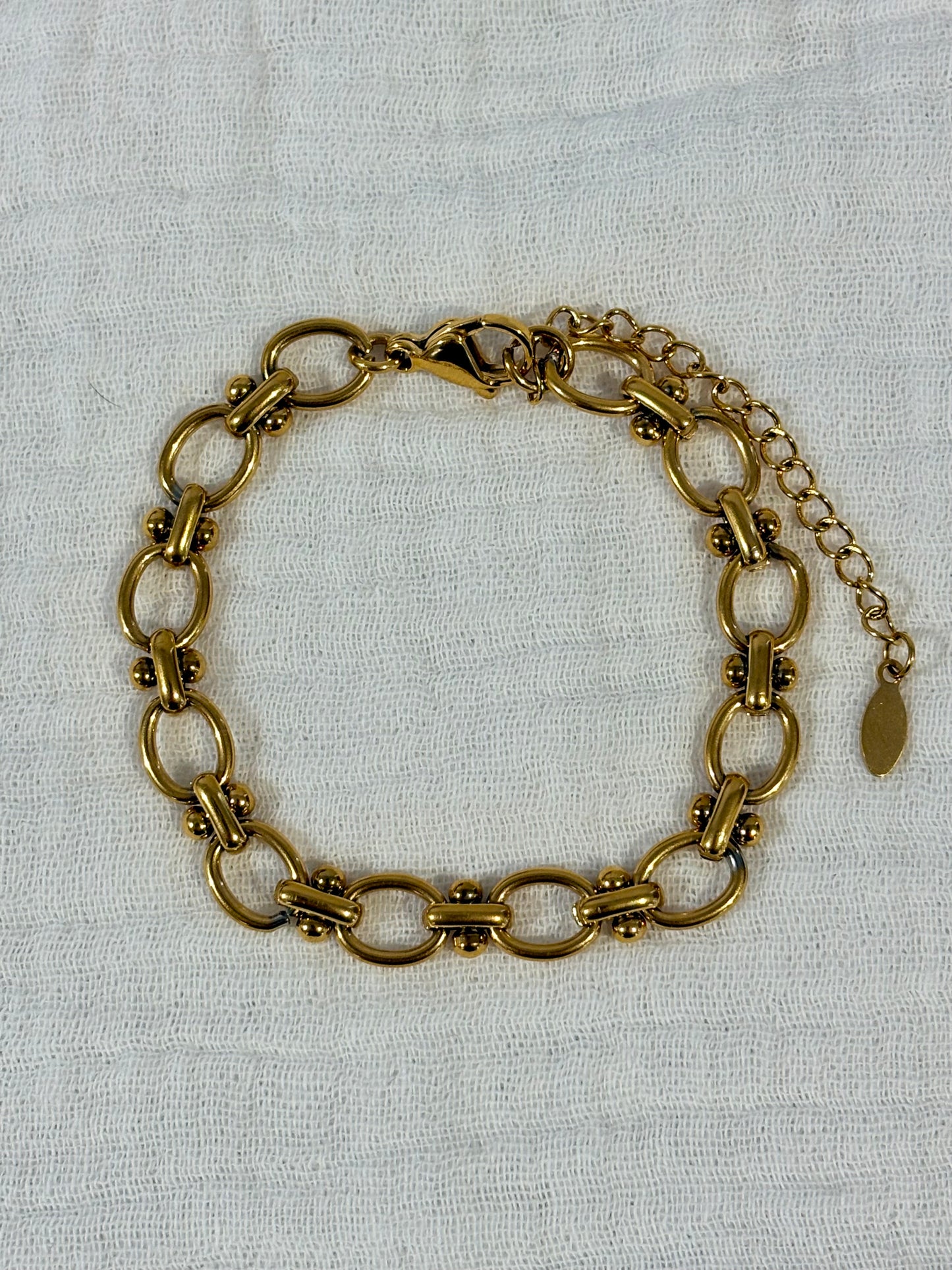 A vintage-style gold-toned chain link bracelet with a lobster clasp and extender chain, displayed on a textured off-white fabric background.