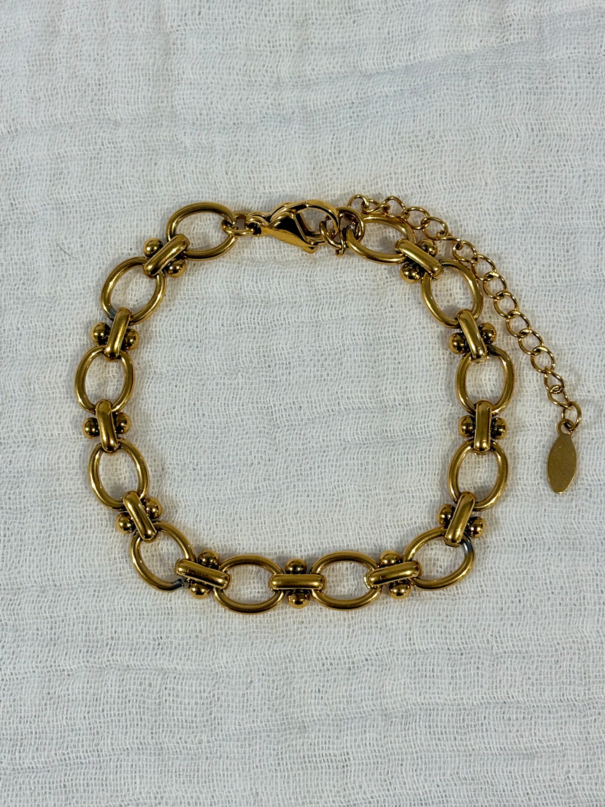 A vintage-style gold-toned chain link bracelet with a lobster clasp and extender chain, displayed on a textured off-white fabric background.