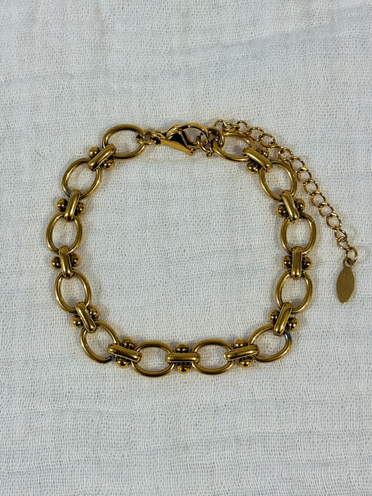 A vintage-style gold-toned chain link bracelet with a lobster clasp and extender chain, displayed on a textured off-white fabric background.
